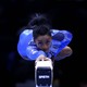 The gymnast Simone Biles lies stretched-out atop a balance beam wearing a shiny blue leotard