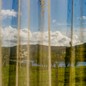 a view of mountains and grass through a curtain