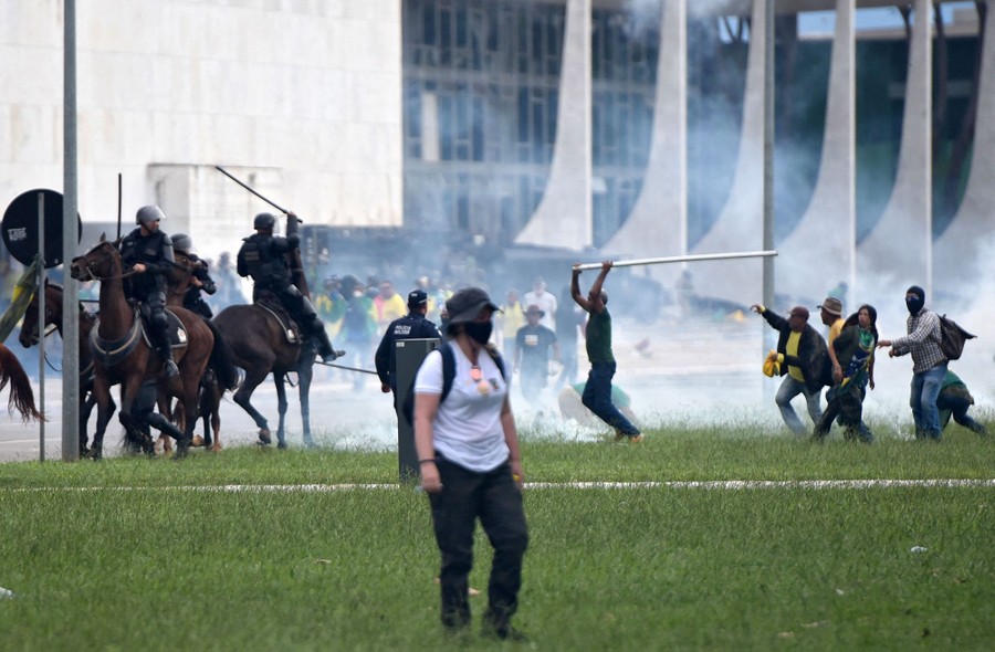 Protesters, one holding what looks like a long pipe, run toward mounted police officers who wield long batons.