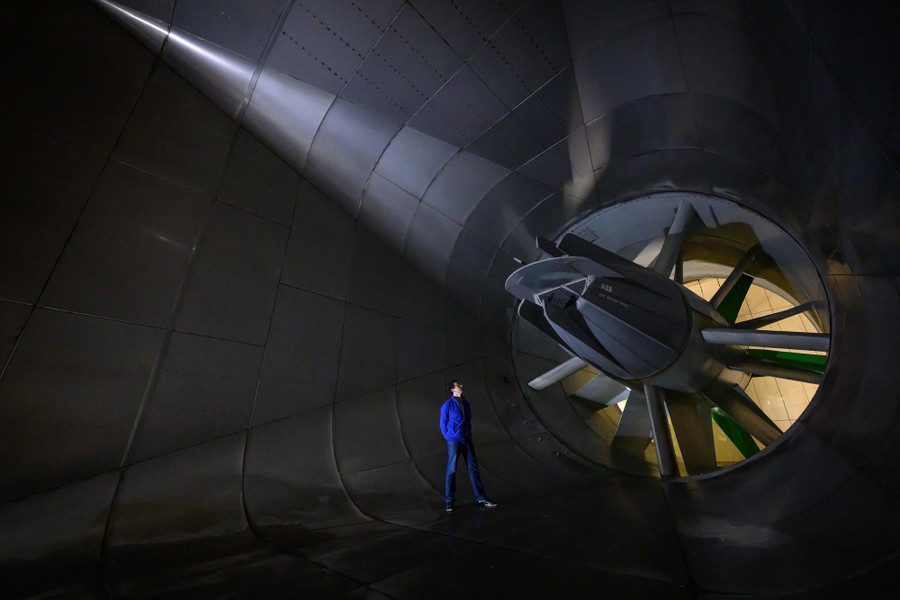A person poses beside an enormous fan inside a wind tunnel.
