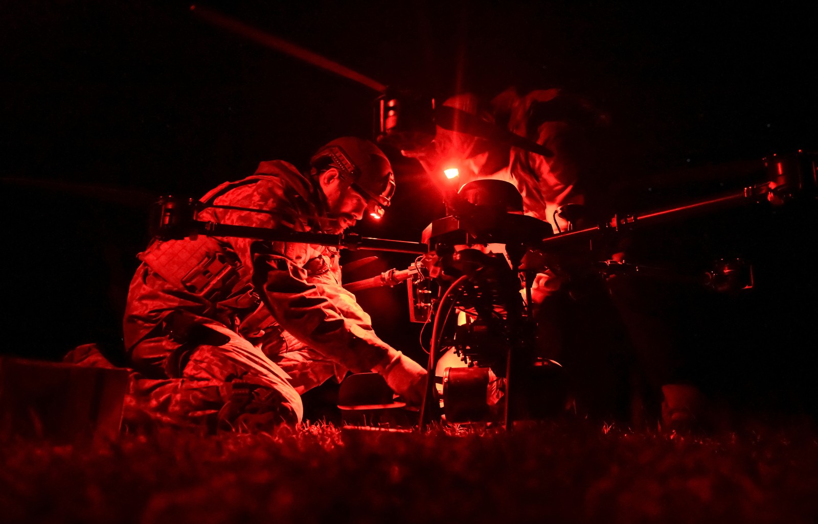 Soldiers kneel down to work with a drone at night.