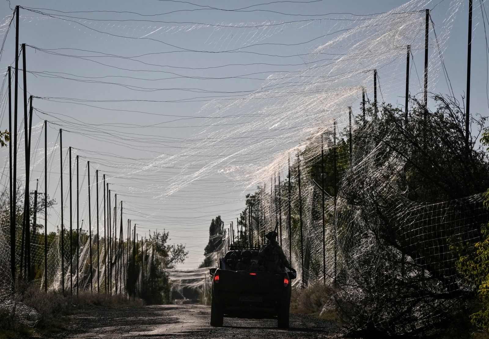 Ukrainian soldiers drive a truck down a road covered in anti-drone netting.
