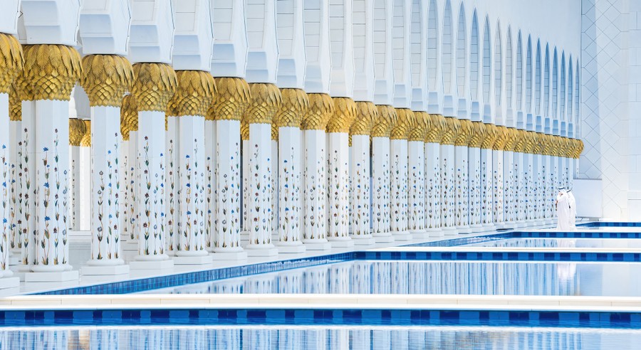 Two men stand beside a long wall of white pillars and several pools of water.