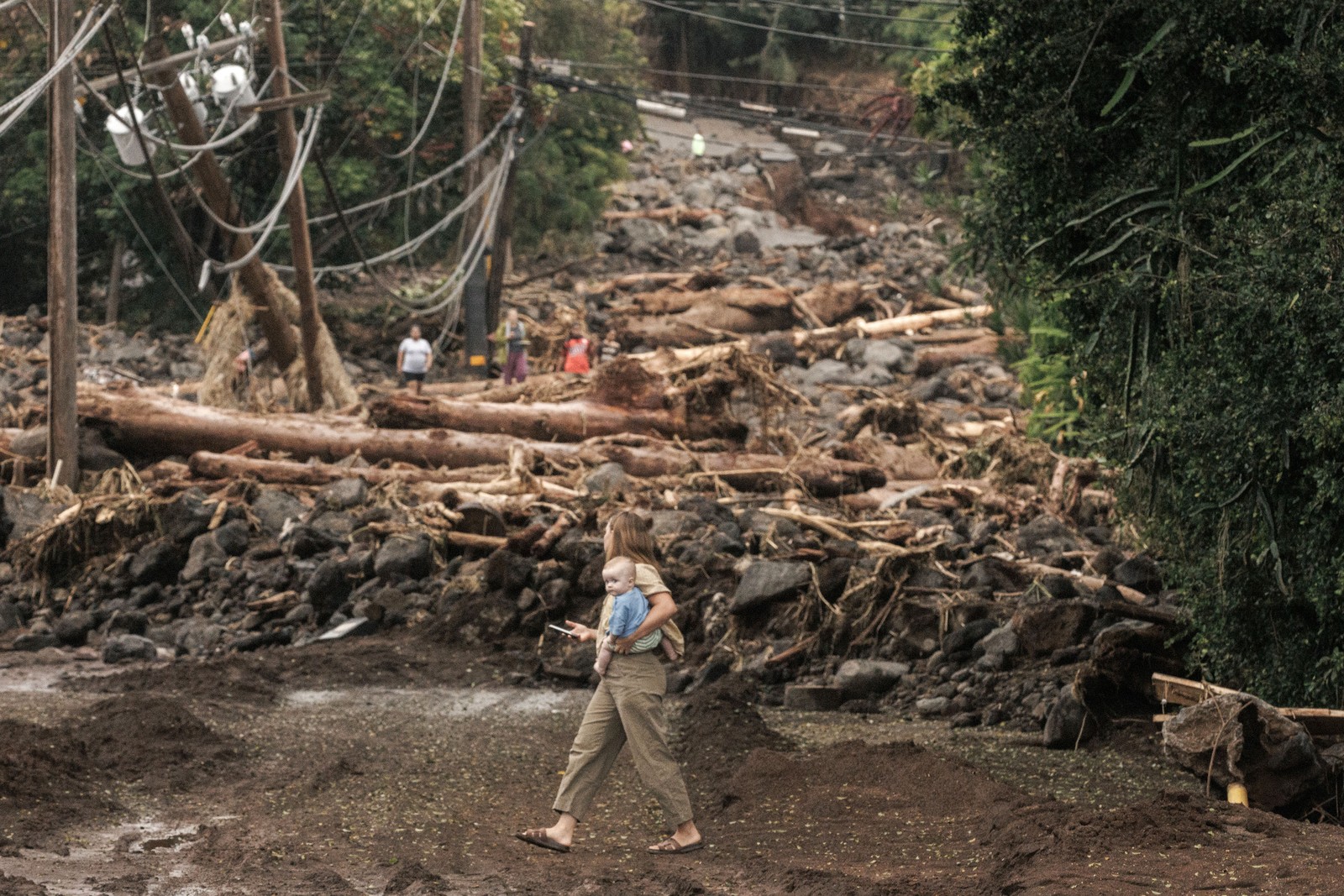 A woman and child walk past a debris-strewn street after a hurricane.
