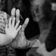 A little girl presses her hand to an old woman's through a glass window