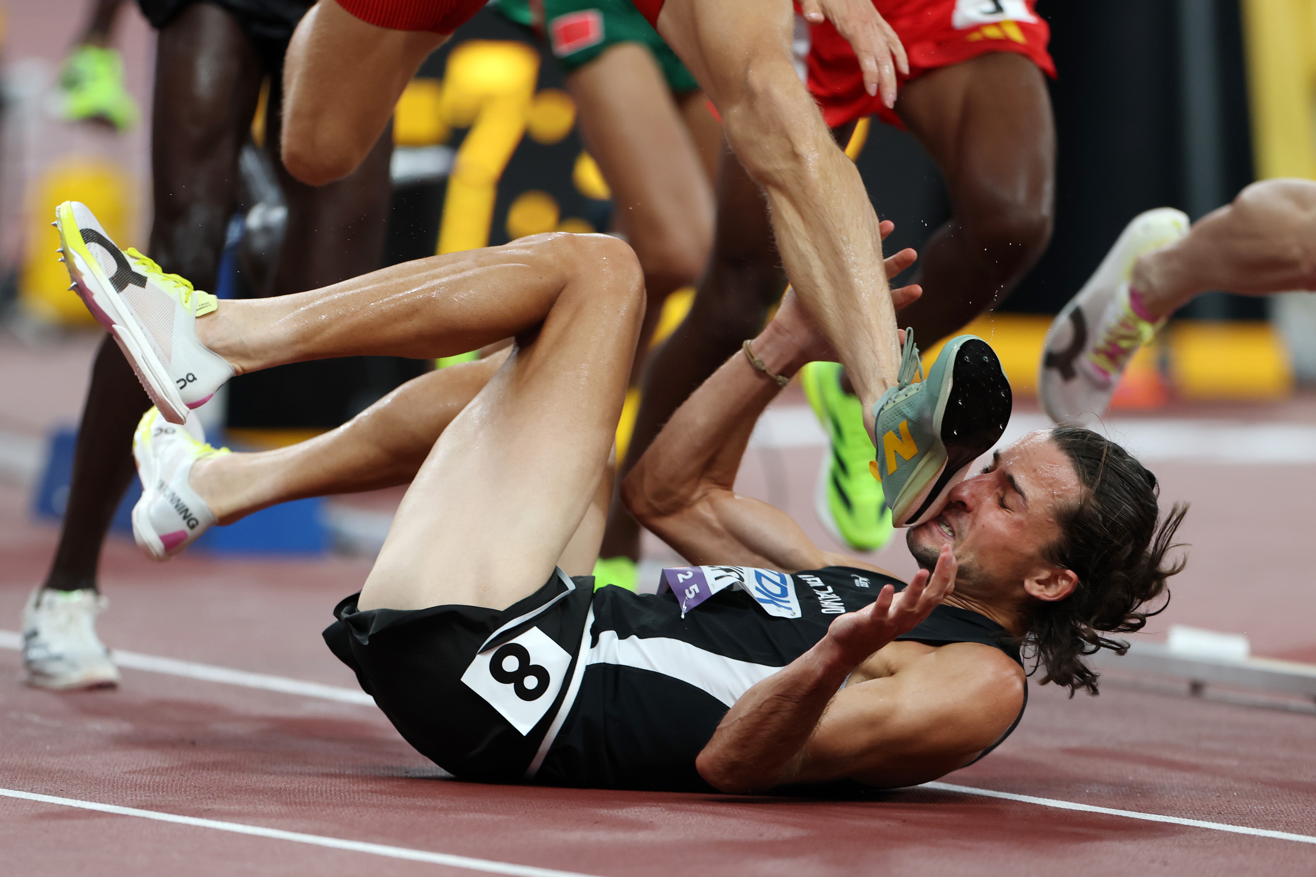 The face of a fallen runner is grazed by the foot of another runner during a race.