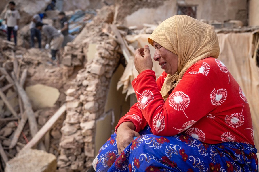 A woman reacts, sitting in the rubble of destroyed buildings.