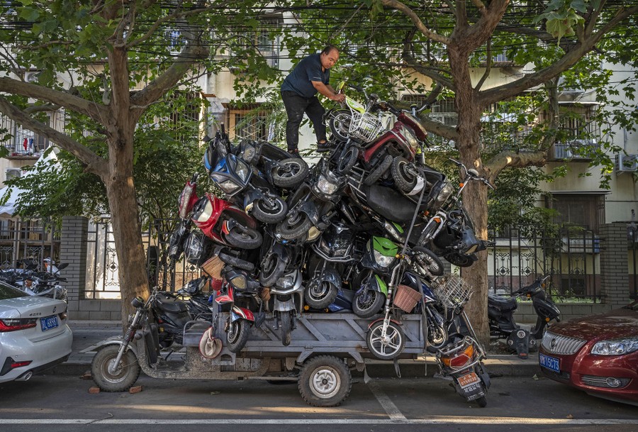 A worker piles salvaged scooters high on a three-wheel truck.