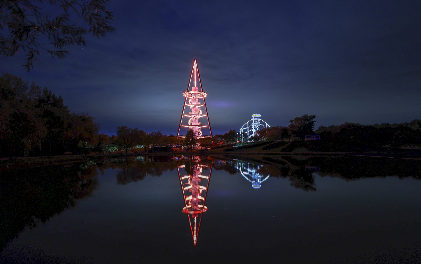 A distant view of an illuminated tall pyramid structure standing beside a lake