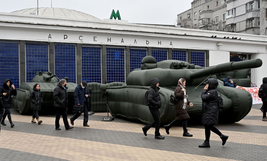 People walk past inflatable tanks placed outside a metro station.