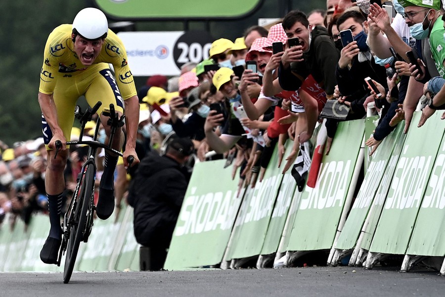 A crowd lines barriers on a road to cheer a passing cyclist.