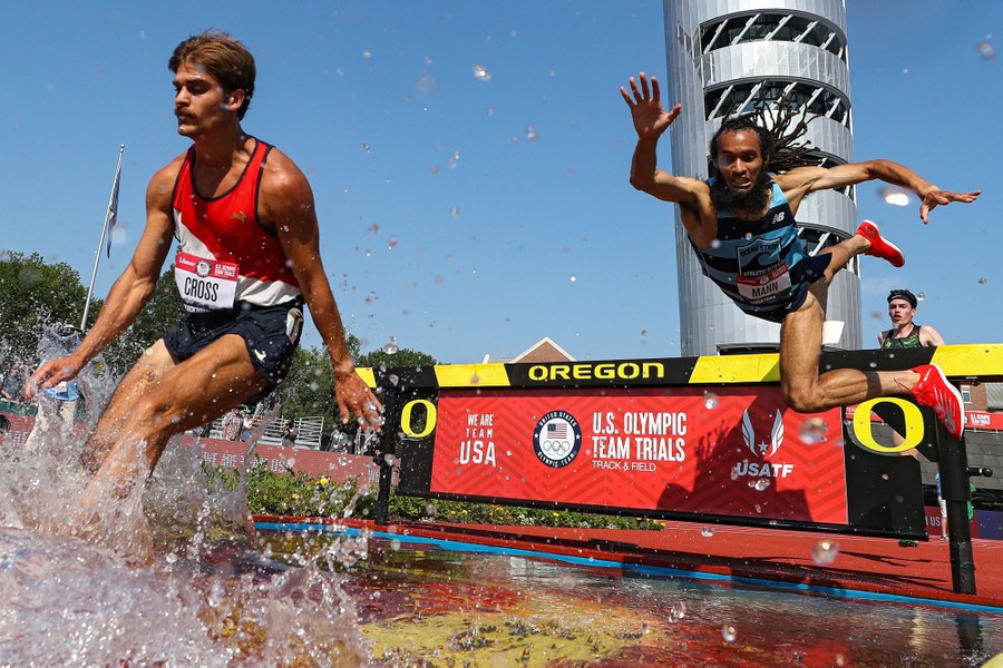 A runner falls over a hurdle as competitors move across a water hazard during a steeplechase run.