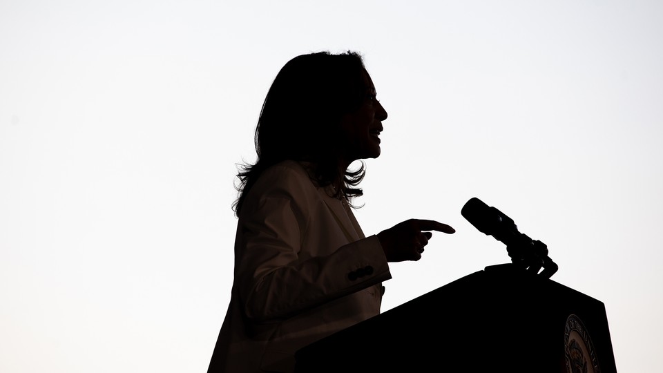 Kamala Harris in shadowy profile standing at a microphone-topped lectern