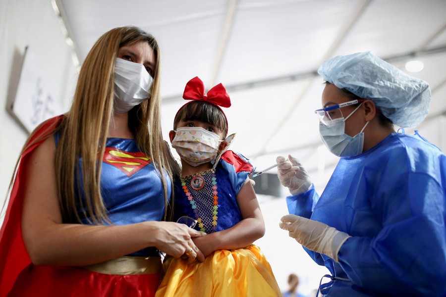 A woman holds a child who is getting a vaccine shot.