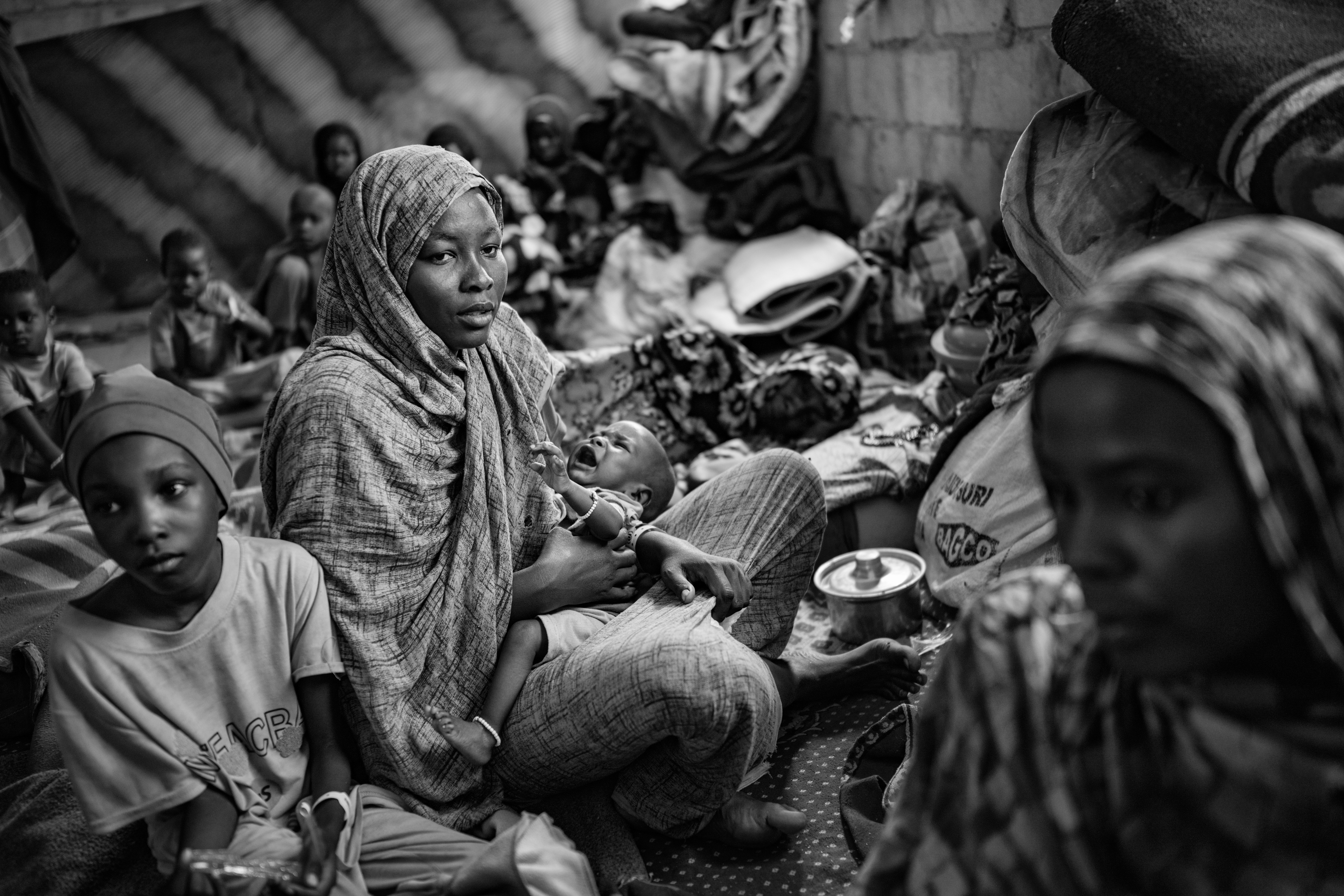 Picture of Taysir Ibrahim Juma, 30, holding her two-month-old son, Mujahid, as she sits among relatives and other Sudanese refugees. 