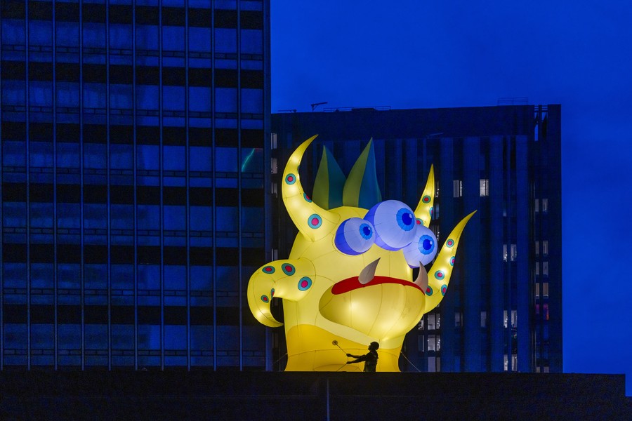 A rigger installs a giant inflatable monster atop a building.