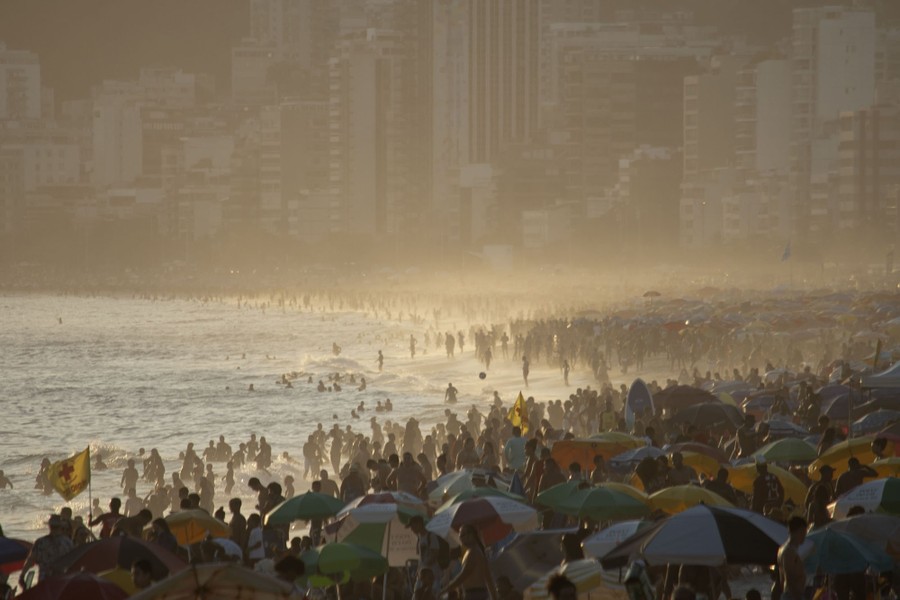 Many people crowd a beach in front of buildings.