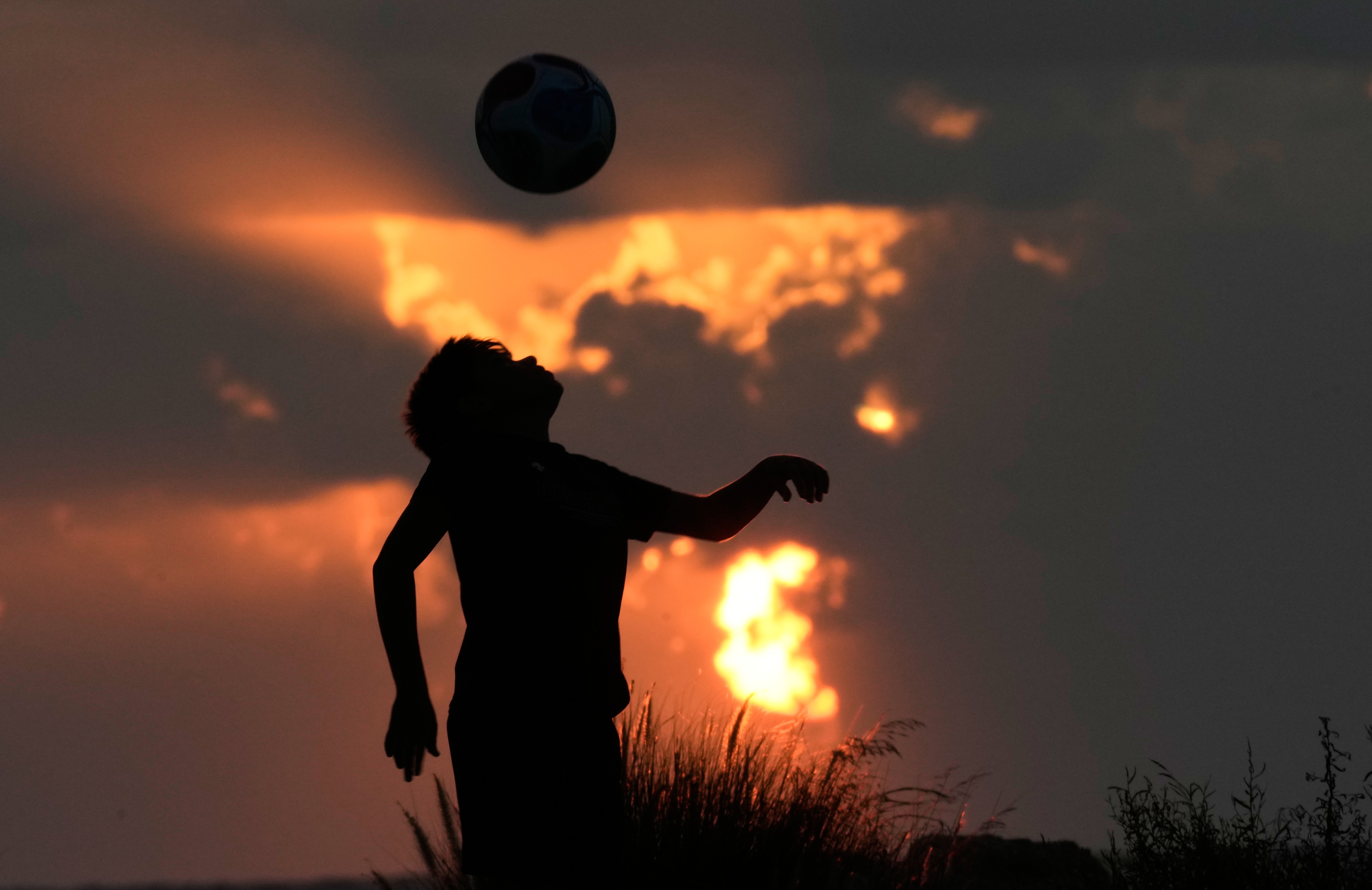 A boy plays soccer as the sun sets.