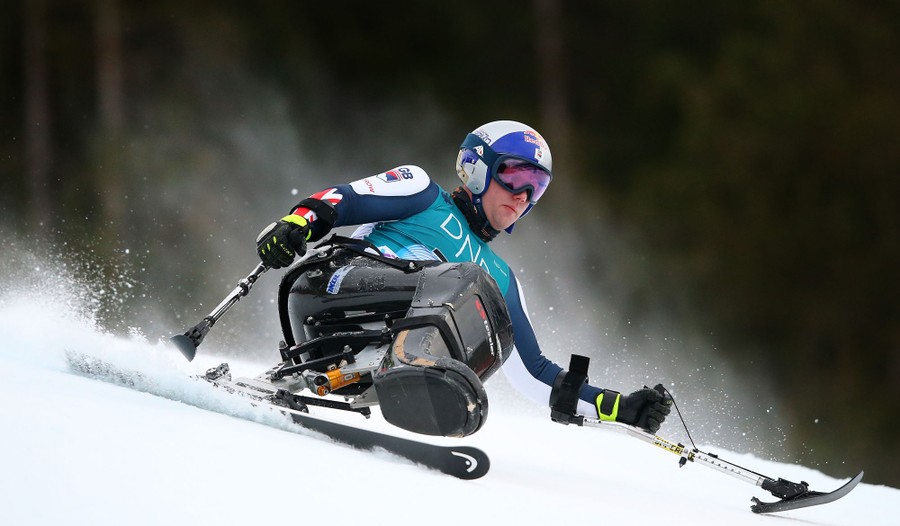 A man races a down a snow-covered hill, seated in a monoski—a plastic shell that protects his legs, mounted on a single ski.