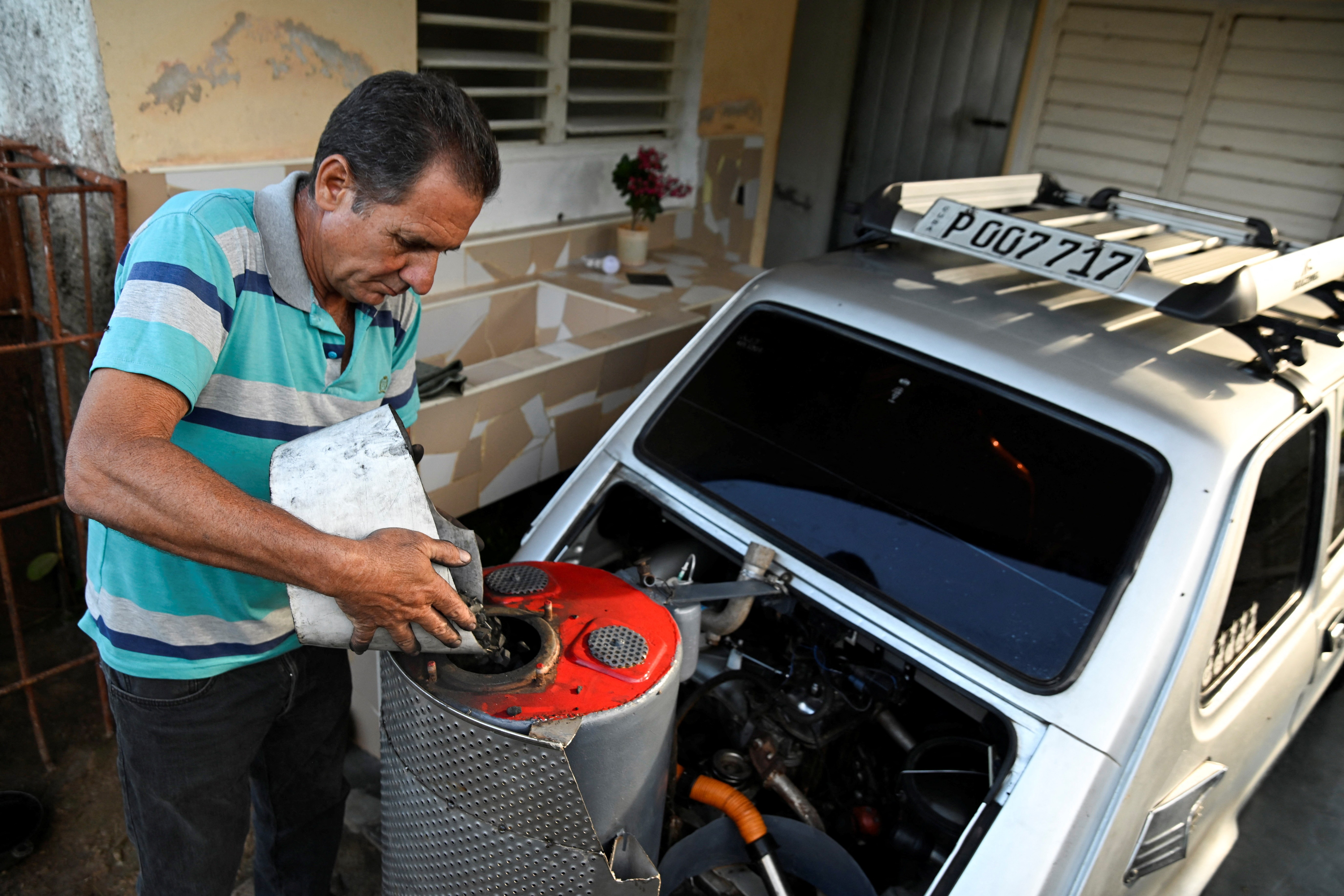 A person puts charcoal into the fuel tank of a car modified to use charcoal instead of gasoline.