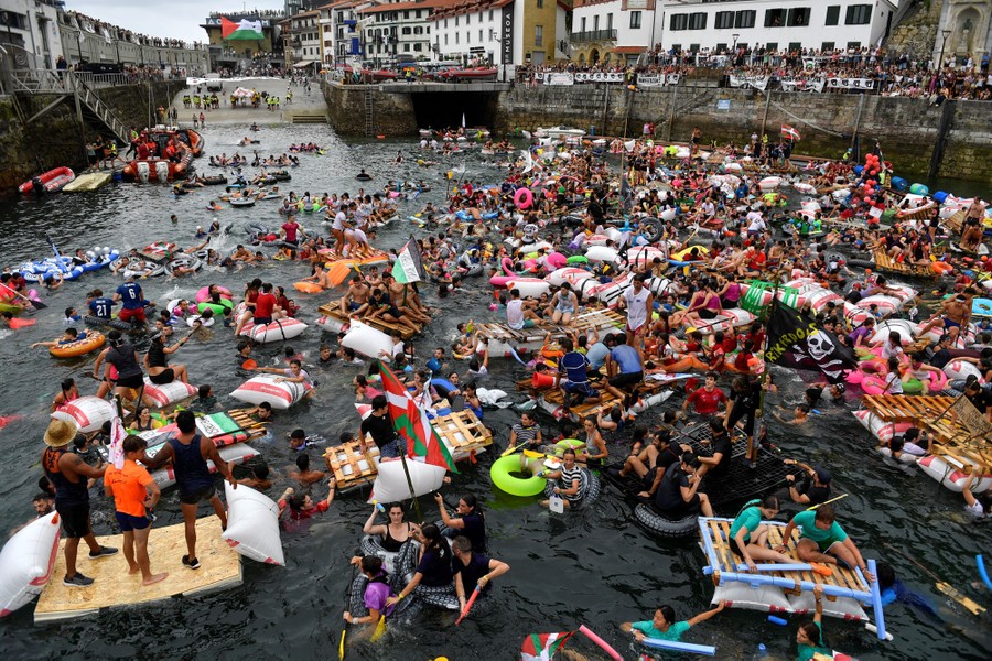 Hundreds of people swim and ride on makeshift rafts and floating devices, filling a small harbor.