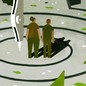 Two people stand in a forest setting, staring at a dark figure. A drafting compass draws circles around them, revealing the landscape.