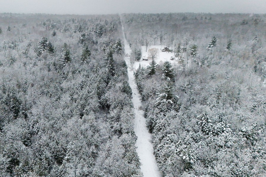 A drone view shows a long, narrow strip of open space cut through a forest, all covered in snow.