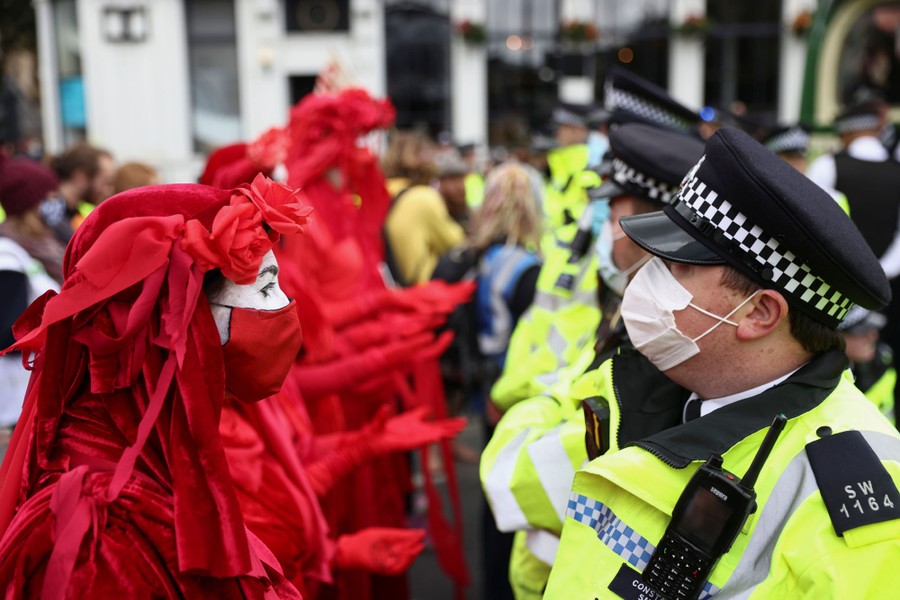 Protesters in costume stand in a line, facing a line of police officers.