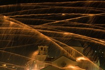 Streaks of light in the night sky above a church, evidence of several firework rockets flying past.