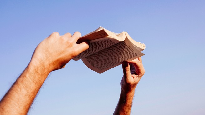 Deux mains tiennent un livre de poche ouvert contre le ciel.