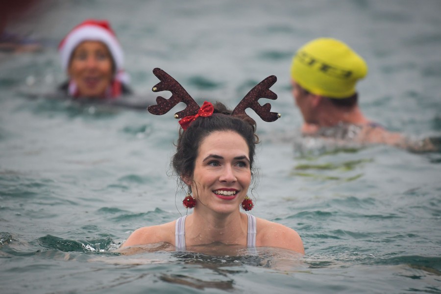 Several people are seen swimming in a harbor; the one at center wears reindeer horns.