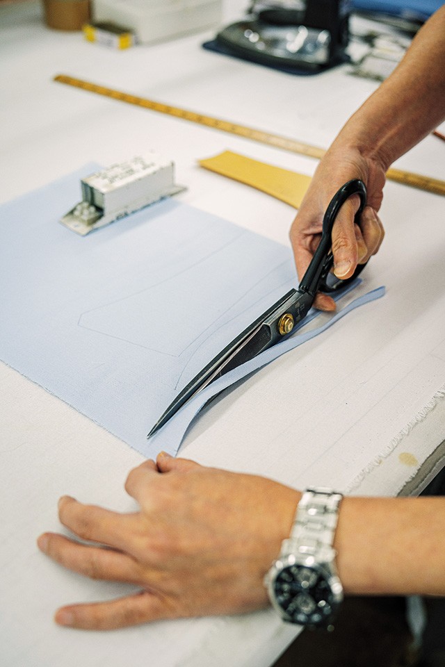 photo of hands cutting a piece of fabric with a scissors on a work table