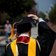 The back of a graduation in a cap and gown. He is talking on his cell phone. 