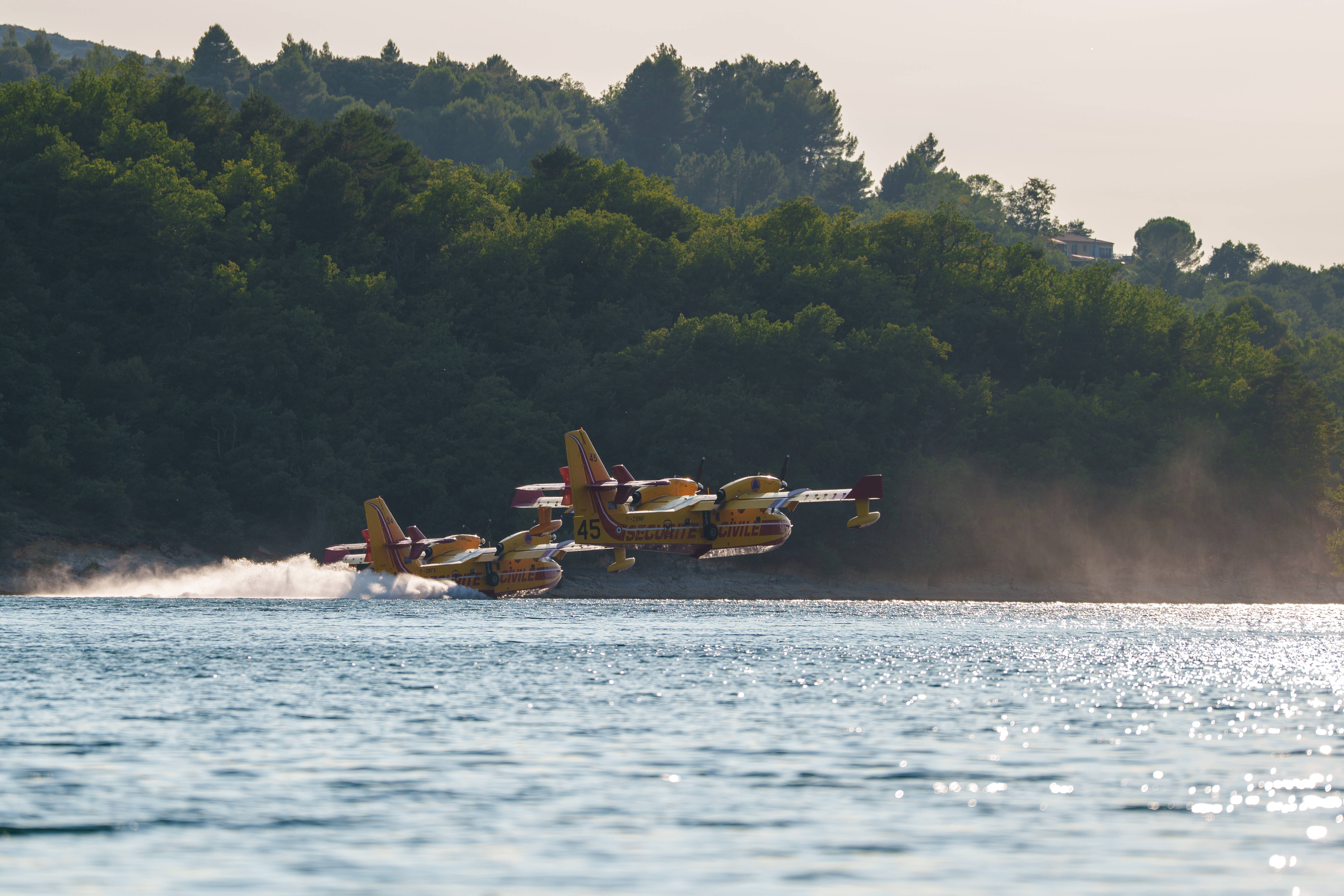 Two firefighting aircraft scoop water from a lake.