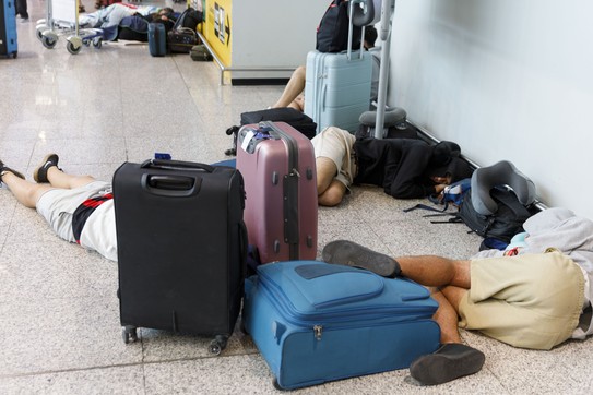 people sprawled out on an airport floor, along with carry-on suitcases