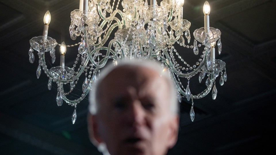 A photo of Joe Biden, blurred in foreground, in front of a chandelier in focus behind.