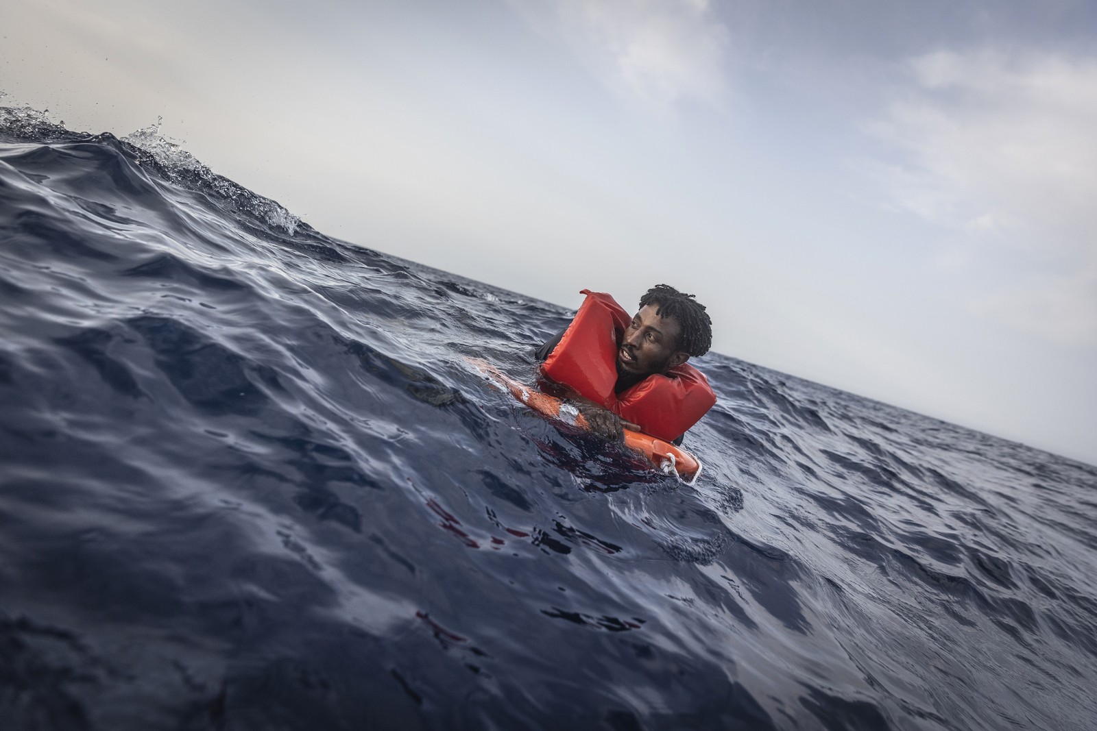 A person wearing a life jacket floats in an open area of ocean.