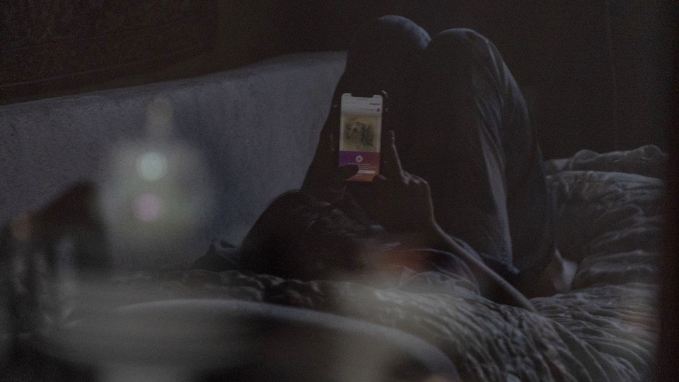 A teenager lying on a couch, looking at a cell phone.