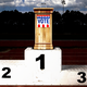 A dais with a "vote" sign sitting atop a winner's podium on a running track