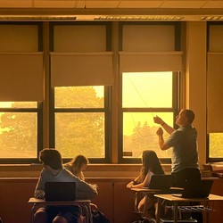 A teacher closes the shades of windows looking out on a haze of wildfire smoke.