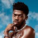Lil Nas X shirtless in bedazzled jewelry against a blue sky