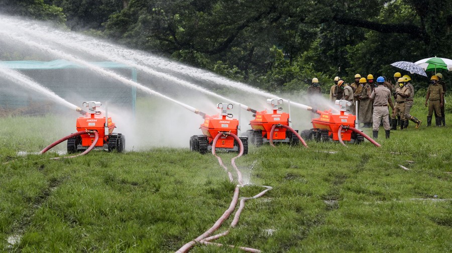 Four small robotic machines blast streams of water as a group of people watch.