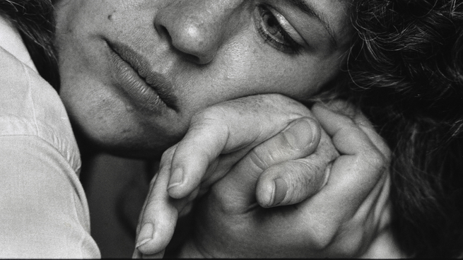 Une femme au visage contemplatif tient la main de quelqu'un d'autre dans la sienne.  Sa joue repose sur leurs mains jointes.