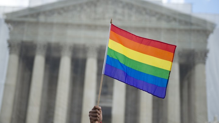 A hand holding a rainbow flag outside of the Supreme Court