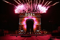 Fireworks erupt from the top of the Arc de Triomphe in Paris, with the number "2024" painted on it in light.