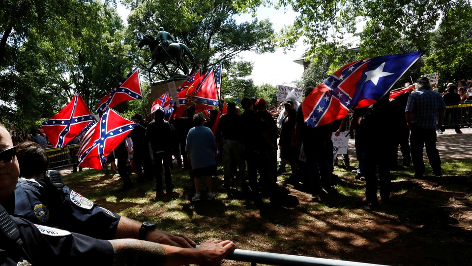 A group surrounds a statue while carrying Confederate flags.