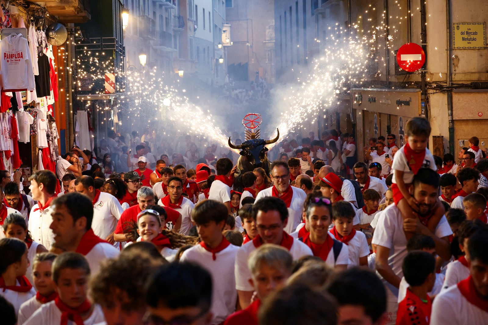 A crowd of festivalgoers runs from a mock fighting bull that is throwing off sparks.