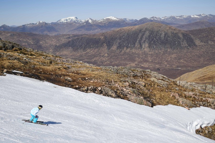 A person skis on a large patch of snow among bare mountains.