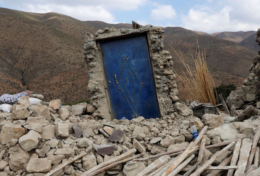 All that remains of a destroyed stone house is a blue door and its frame, standing among piles of rubble.