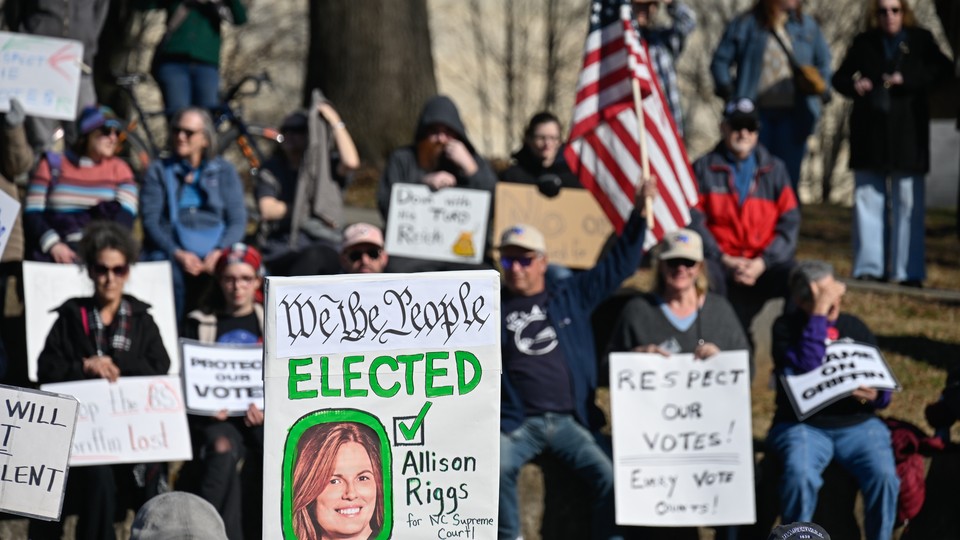 A group of protesters gather in North Carolina. One sign reads: We the People elected Allison Riggs for NC Supreme Court
